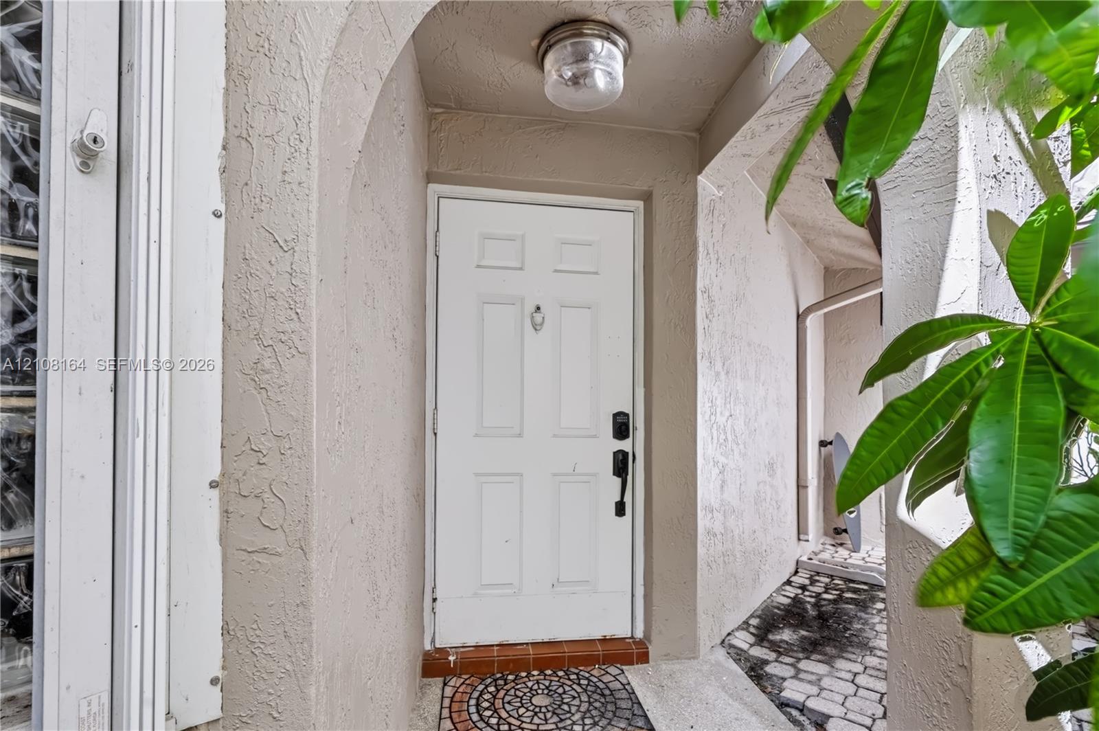 Covered entryway featuring a recessed arched alcove, a multi-panel white entry door with a brass-finish knocker, and a decorative circular mosaic tile inlay at the threshold