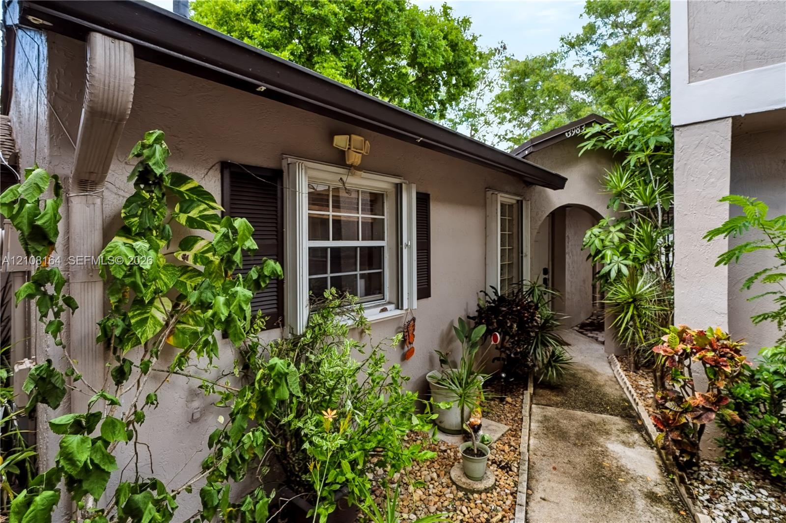 Stucco exterior featuring dual-pane windows with dark shutters, a covered arched entryway, and a stone-lined walkway