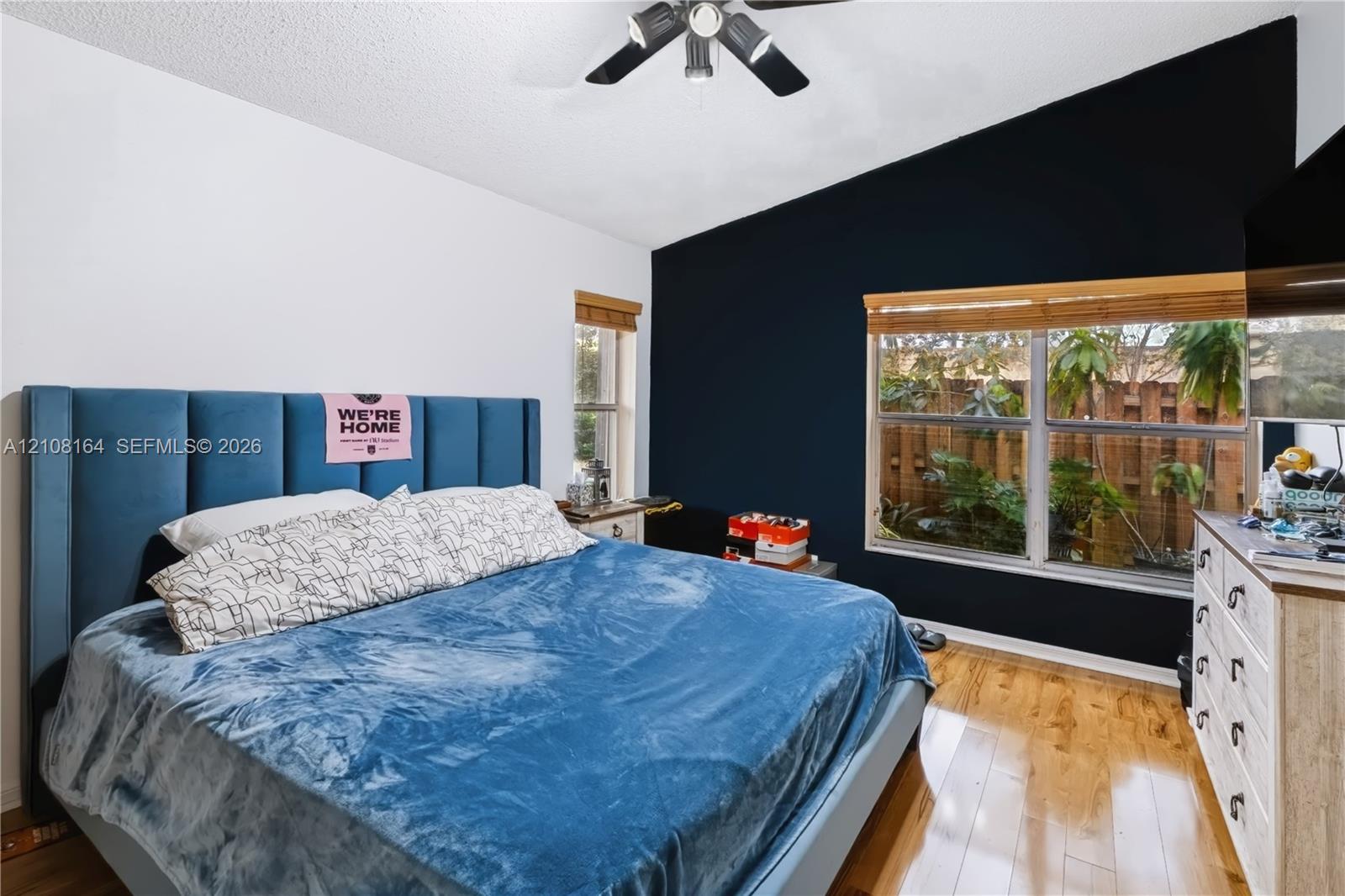 Room featuring a vaulted ceiling, wood-finish flooring, dual-pane windows, and a multi-blade ceiling fan with integrated lighting
