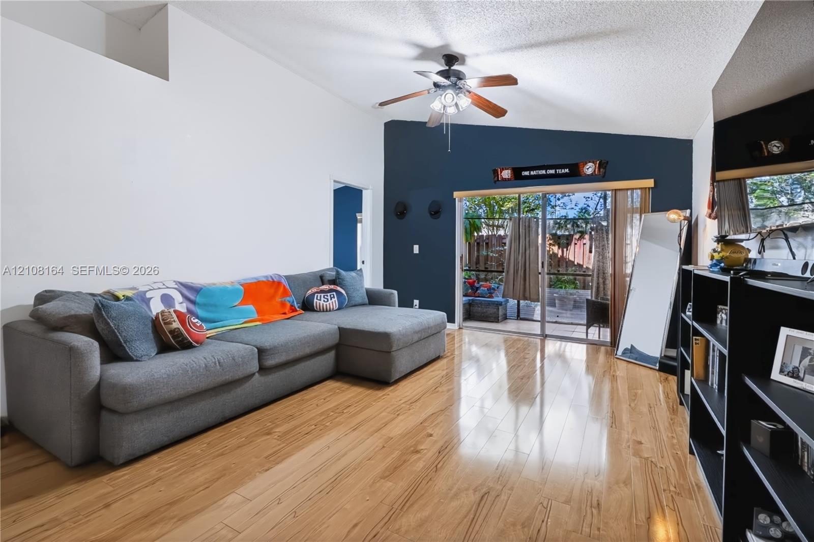 Vaulted ceiling with an integrated ceiling fan, wood-finish flooring, and sliding glass doors providing exterior access