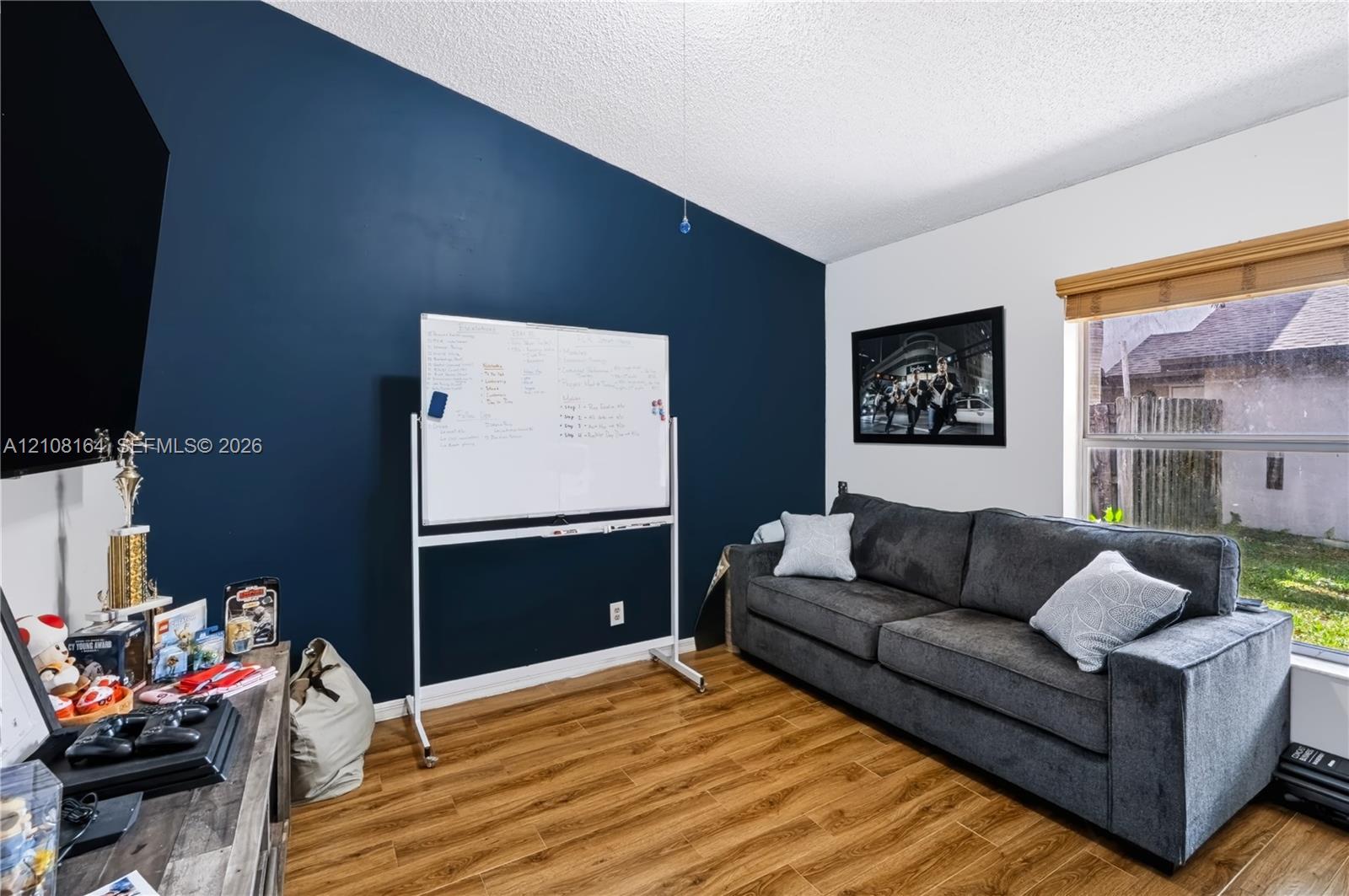 Room featuring wood-finish flooring, a bold navy accent wall, and a horizontal window with wood-slat blinds