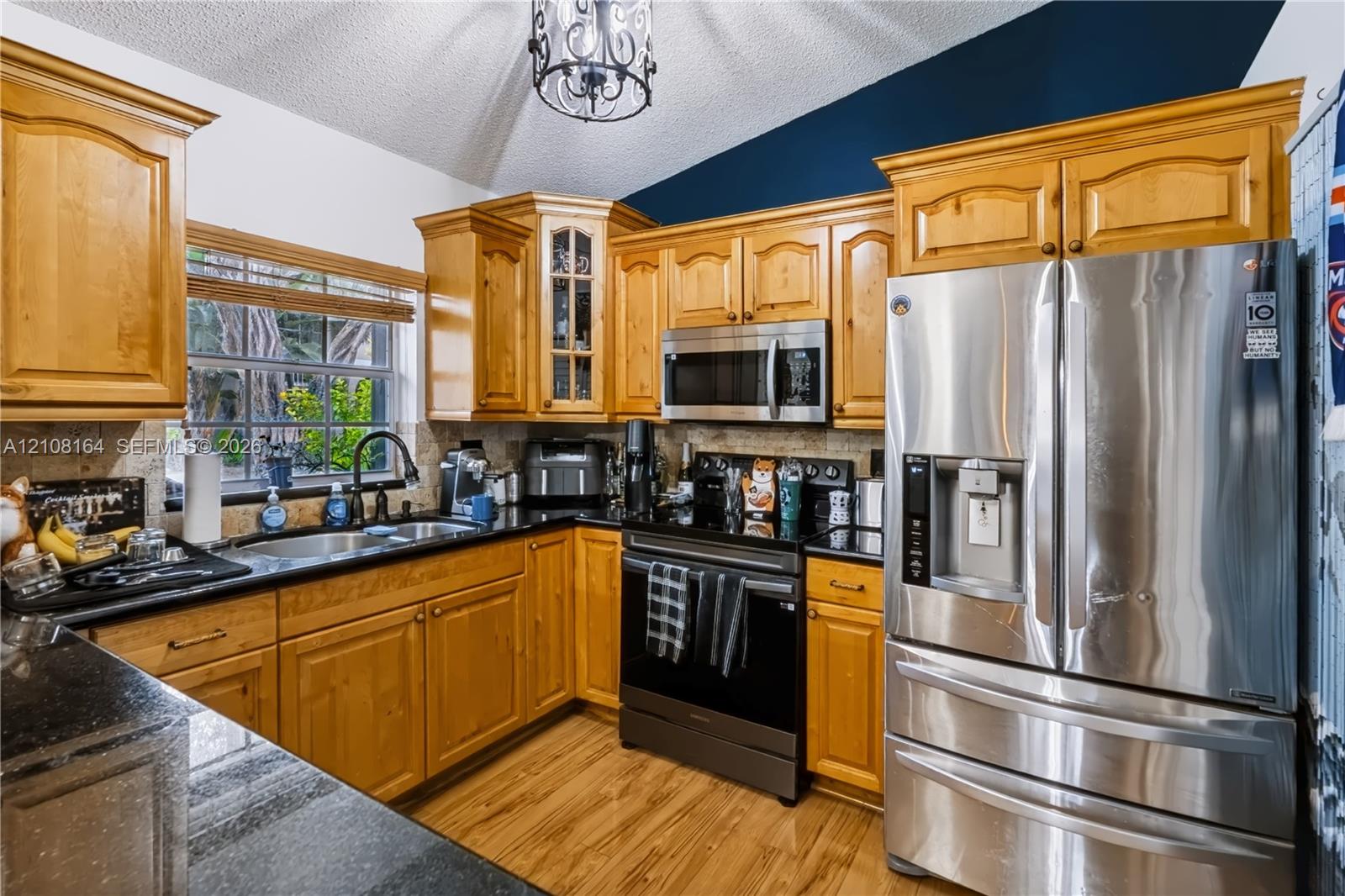 Kitchen featuring wood cabinetry, stone countertops, stainless steel appliances, a vaulted ceiling with a decorative pendant light, and wood-finish flooring