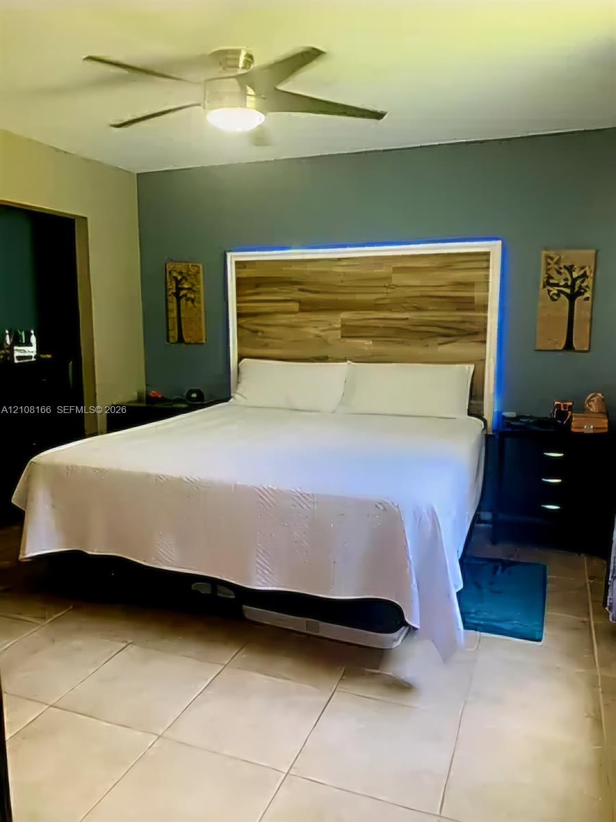 Room featuring large-format tile flooring, a multi-blade ceiling fan with integrated lighting, and a custom wood-finish headboard accent wall with perimeter backlighting