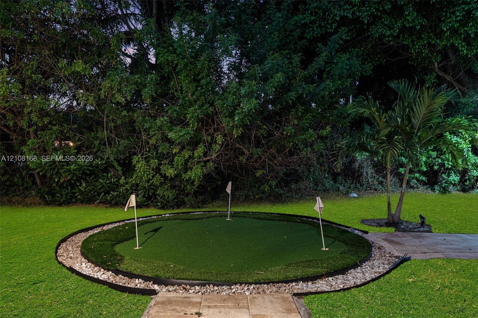 Backyard putting green featuring three flag pins, synthetic turf surface, stone border edging, and stone paver walkway