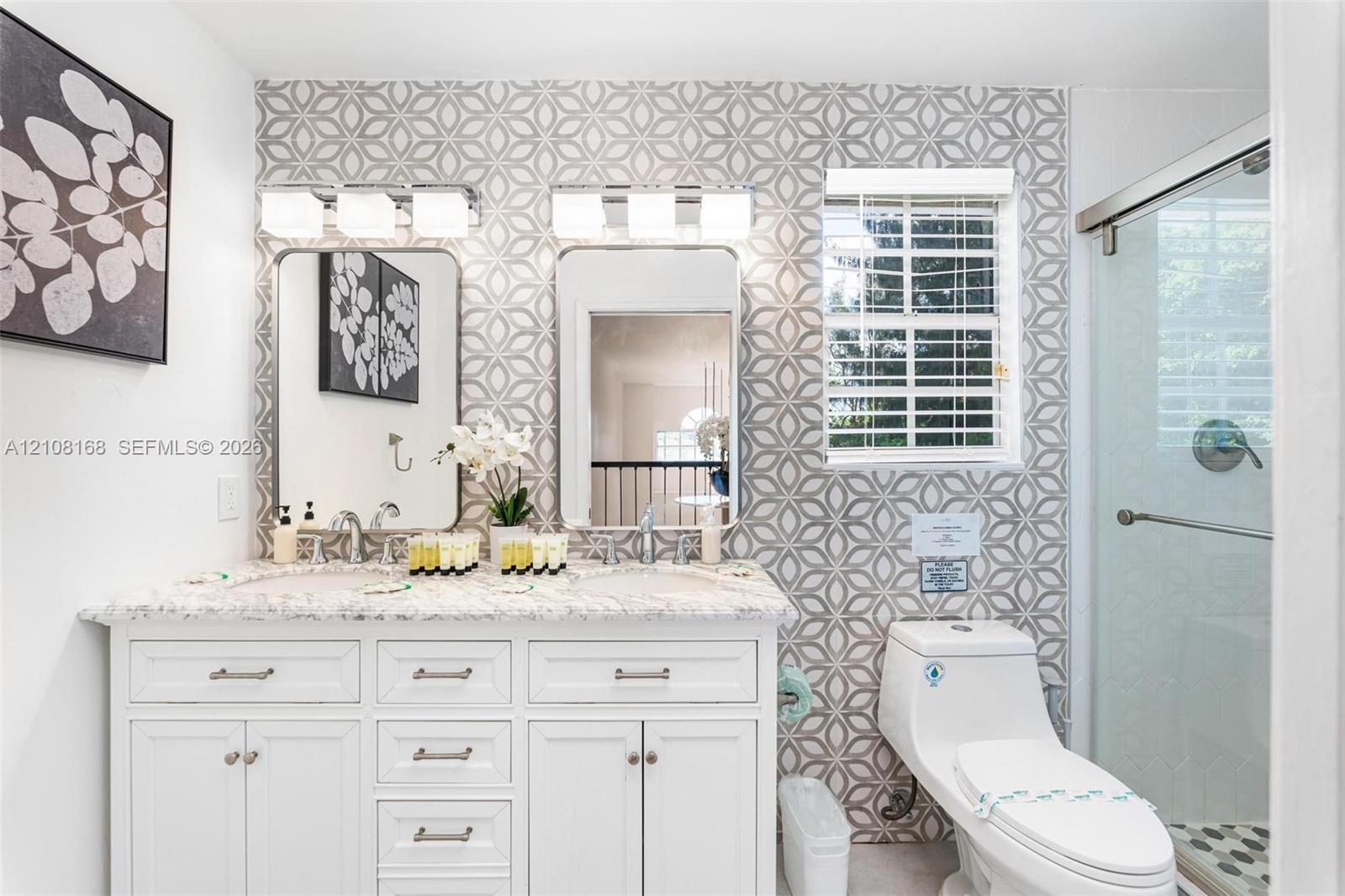 Dual-sink vanity with white cabinetry, patterned tile feature wall, rectangular mirrors, and a glass-enclosed shower