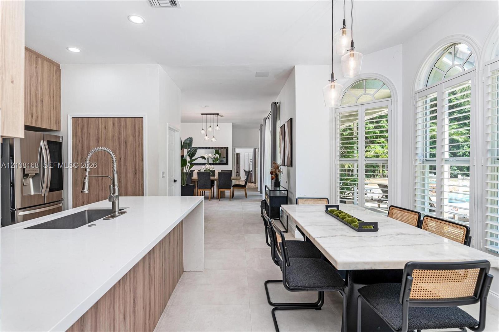 Kitchen featuring a large quartz-topped center island with integrated sink, wood-finish cabinetry, recessed lighting, and expansive arched windows with plantation shutters