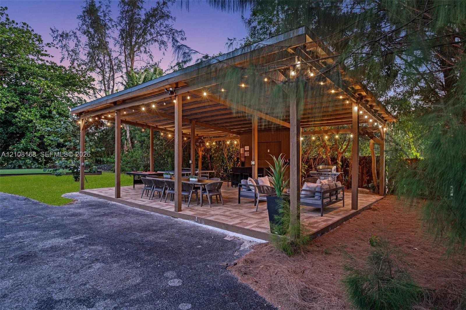 Covered outdoor pavilion featuring a timber-frame structure, exposed ceiling rafters, tile flooring, and integrated string lighting