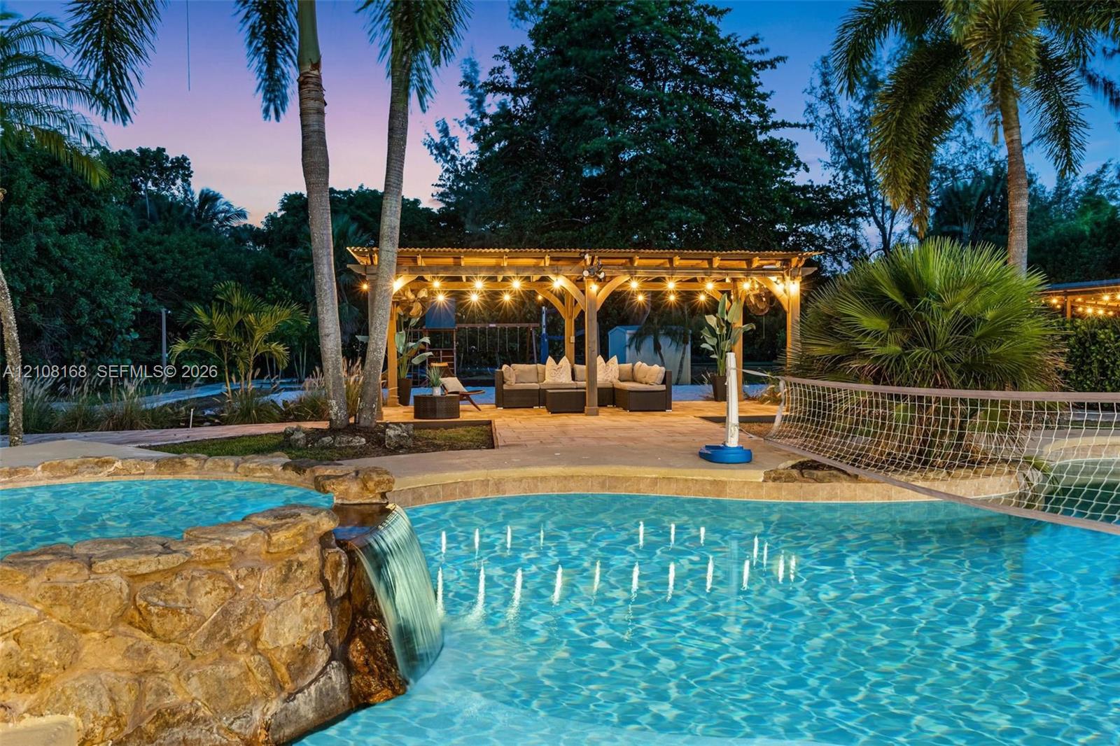 Swimming pool featuring a stacked stone waterfall, custom paver decking, and a wood-frame pergola