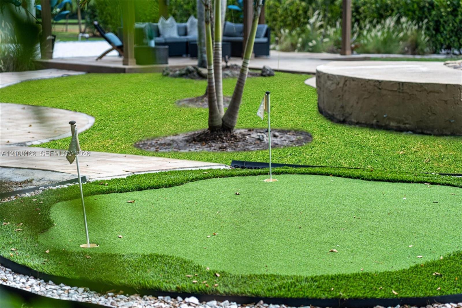 Backyard putting green with synthetic turf, stone-finish hardscaping, mature palm trees, and ground-level concrete edging