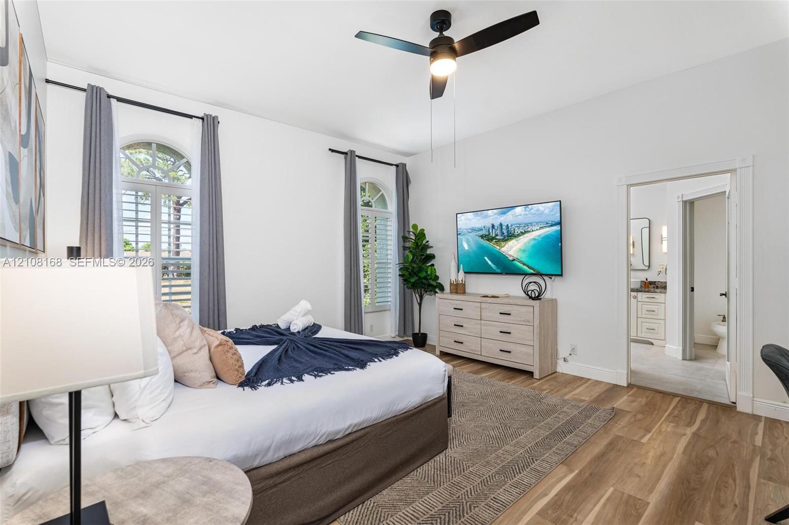Wood-finish flooring, high ceilings with a central fan, and arched windows featuring custom shutters