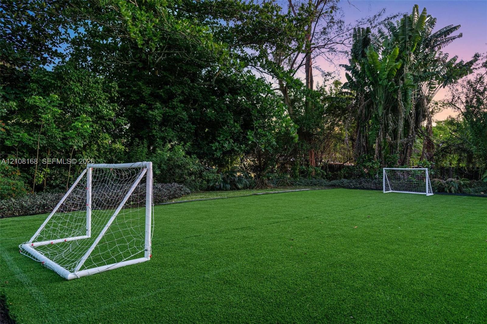 Expansive lawn featuring artificial turf, mature tree border, and perimeter landscaping