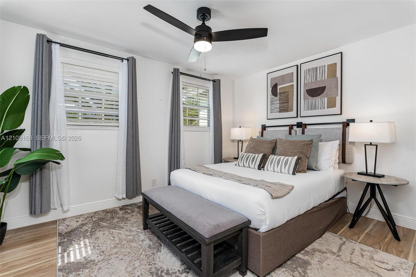 Wood-finish flooring, matte black ceiling fan with integrated lighting, and dual shutter-style windows