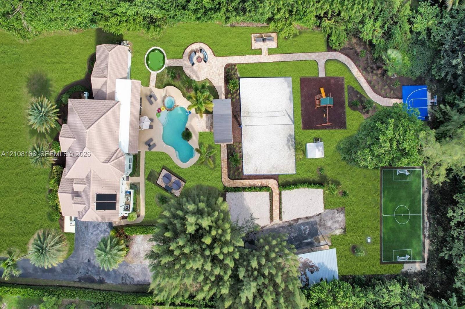 Expansive backyard featuring a custom-shaped swimming pool with an attached spa, a sand volleyball court, a soccer field, a paved walking path, and a fire pit area