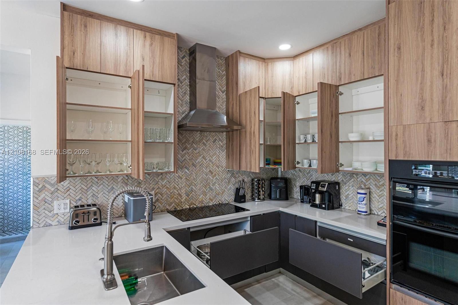 Kitchen featuring custom wood-finish cabinetry, stone-surface countertops, a herringbone-patterned tile backsplash, a stainless steel range hood, and an integrated wall oven