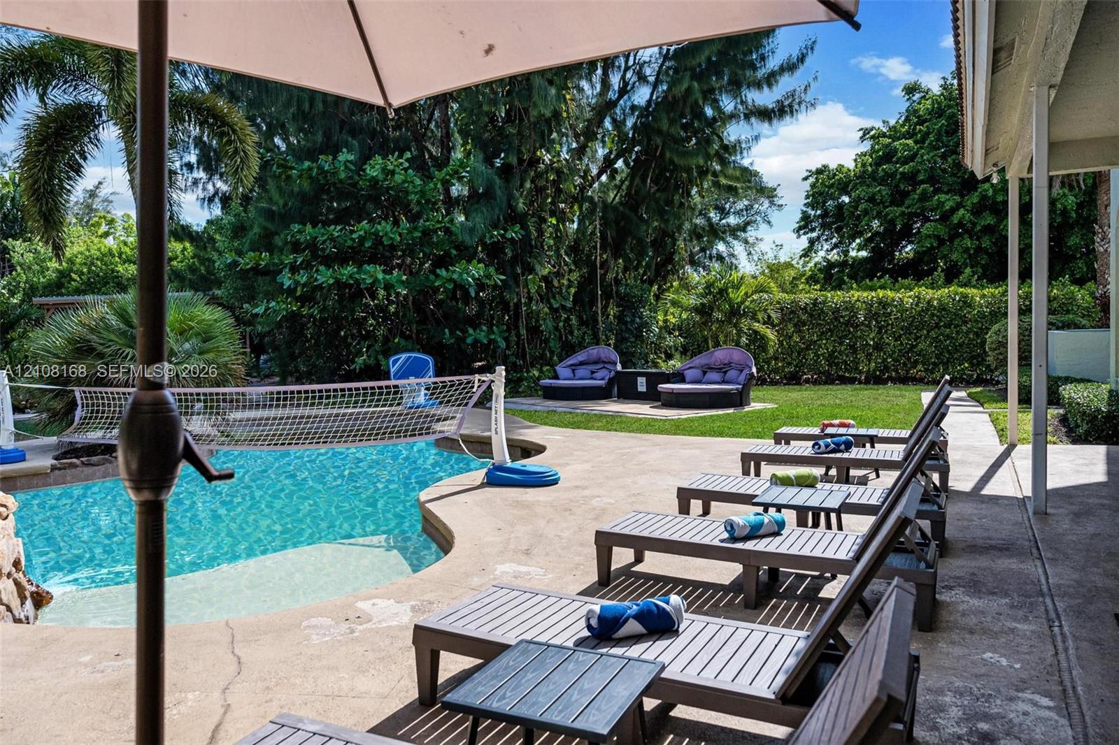 Outdoor area featuring a concrete patio, swimming pool, manicured lawn, and mature perimeter landscaping