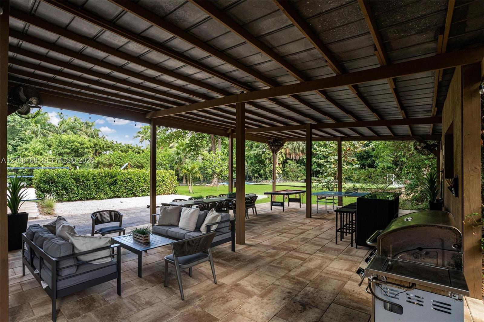 Covered outdoor patio featuring stone-tiled flooring, a stained-wood beam ceiling, and an integrated grilling station