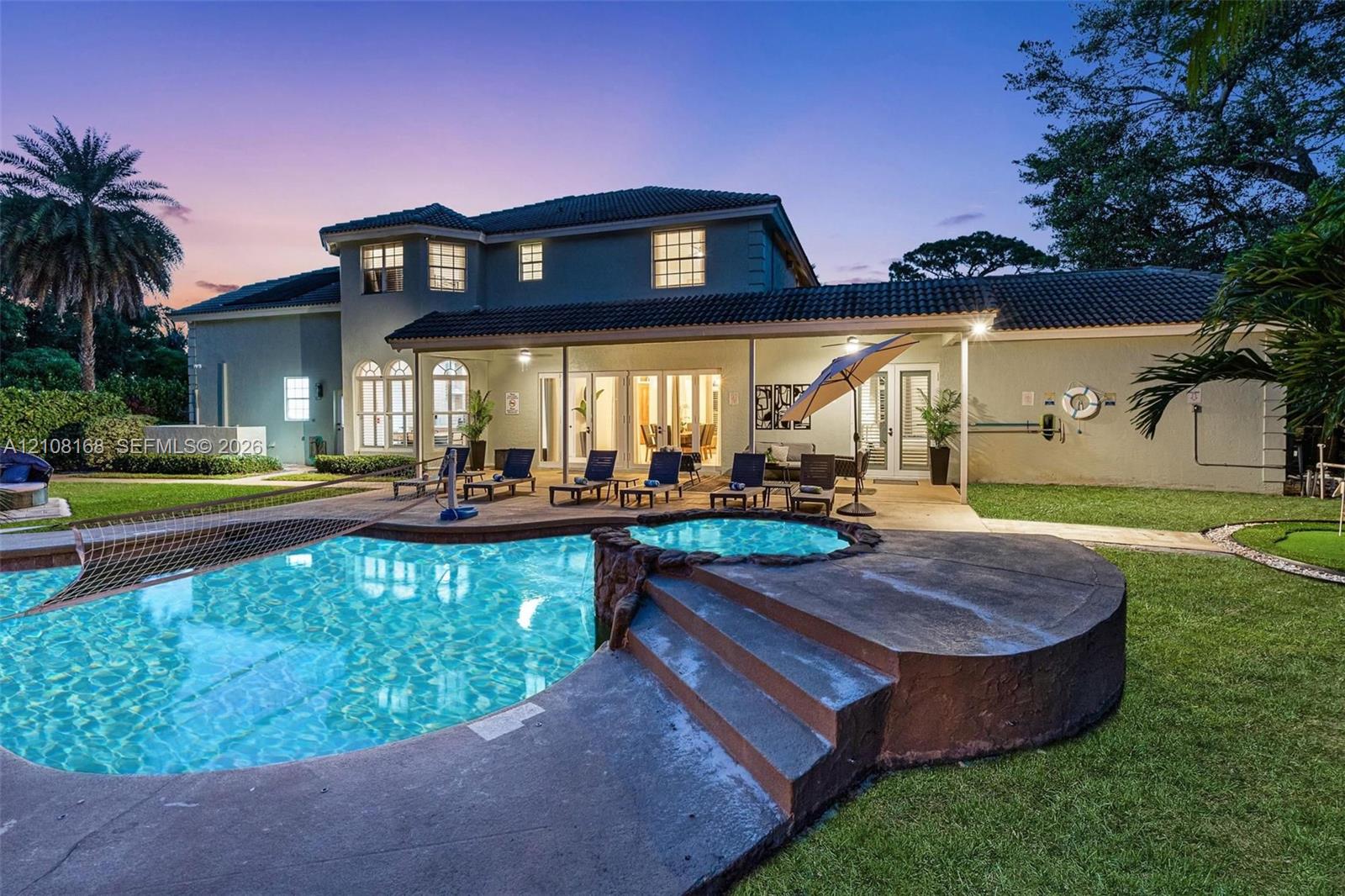 Two-story exterior featuring a hip roof, covered patio, integrated swimming pool with a raised spa, and concrete hardscaping