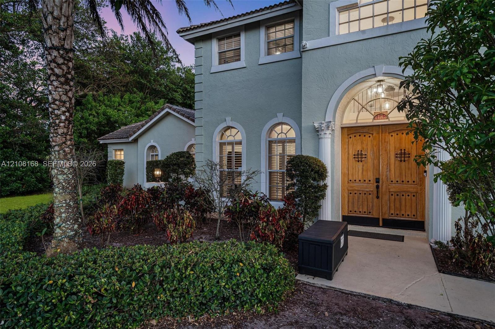 Two-story exterior featuring a stucco facade, tile roof, multi-car garage, asphalt driveway, and mature palm trees