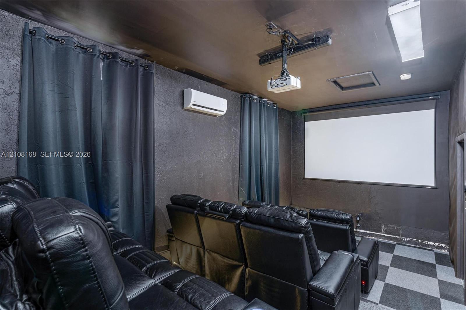 Media room featuring a mounted projection screen, ceiling-mounted digital projector, wall-mounted ductless air conditioning unit, and checkered tile flooring