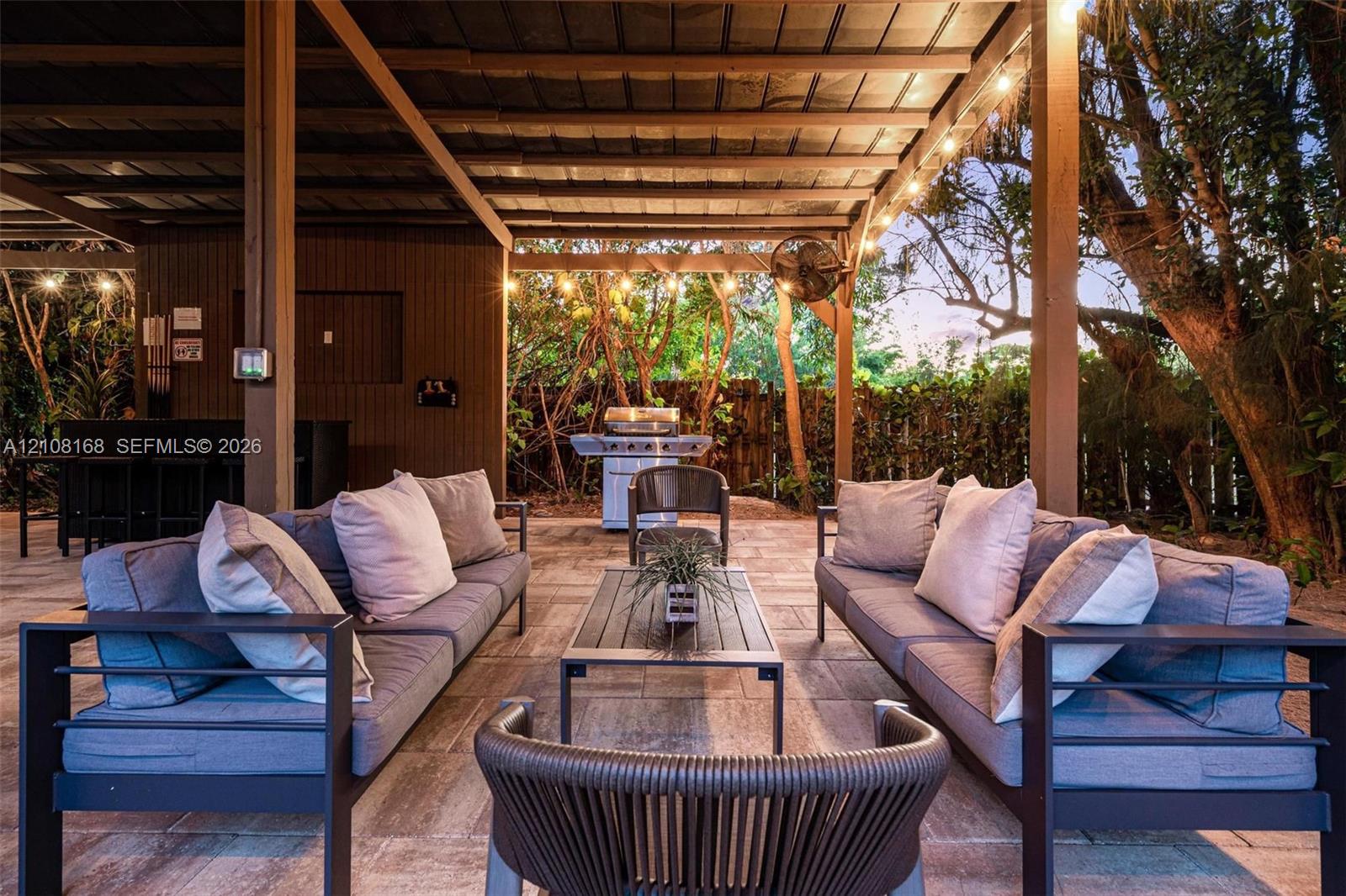 Covered outdoor patio featuring paver flooring, wood-beam ceiling construction, wall-mounted fan, integrated lighting, and a built-in outdoor cooking area