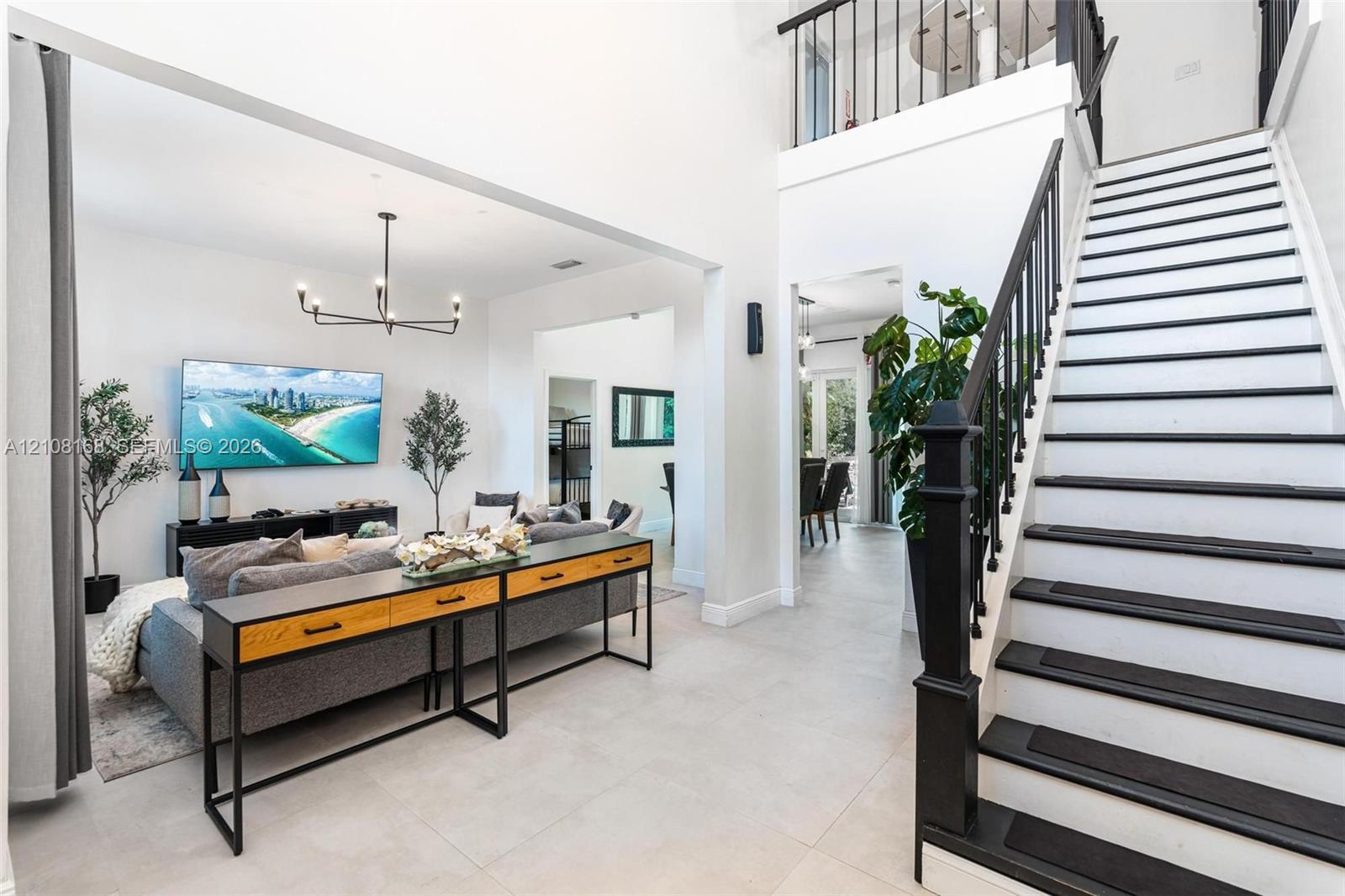 Two-story foyer with high ceilings, large-format tile flooring, a geometric multi-arm chandelier, and a staircase featuring black-painted treads and a metal railing