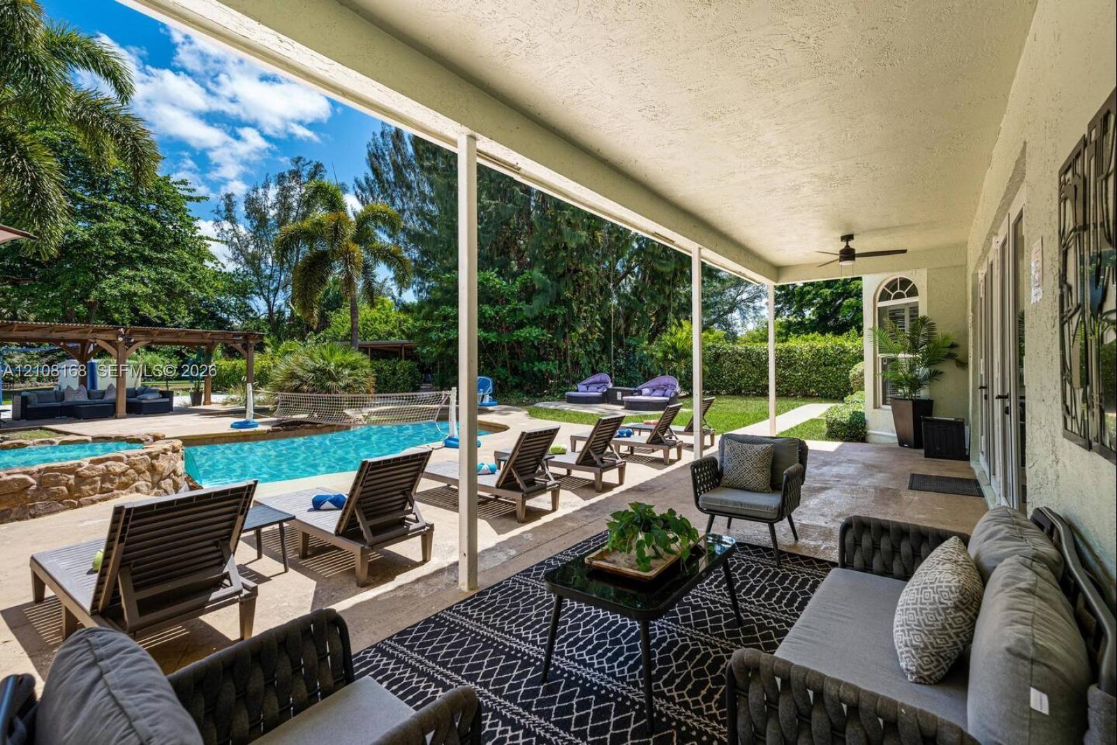 Covered outdoor patio featuring natural stone flooring, a ceiling fan, a swimming pool with rock-style water feature, and a wooden pergola structure