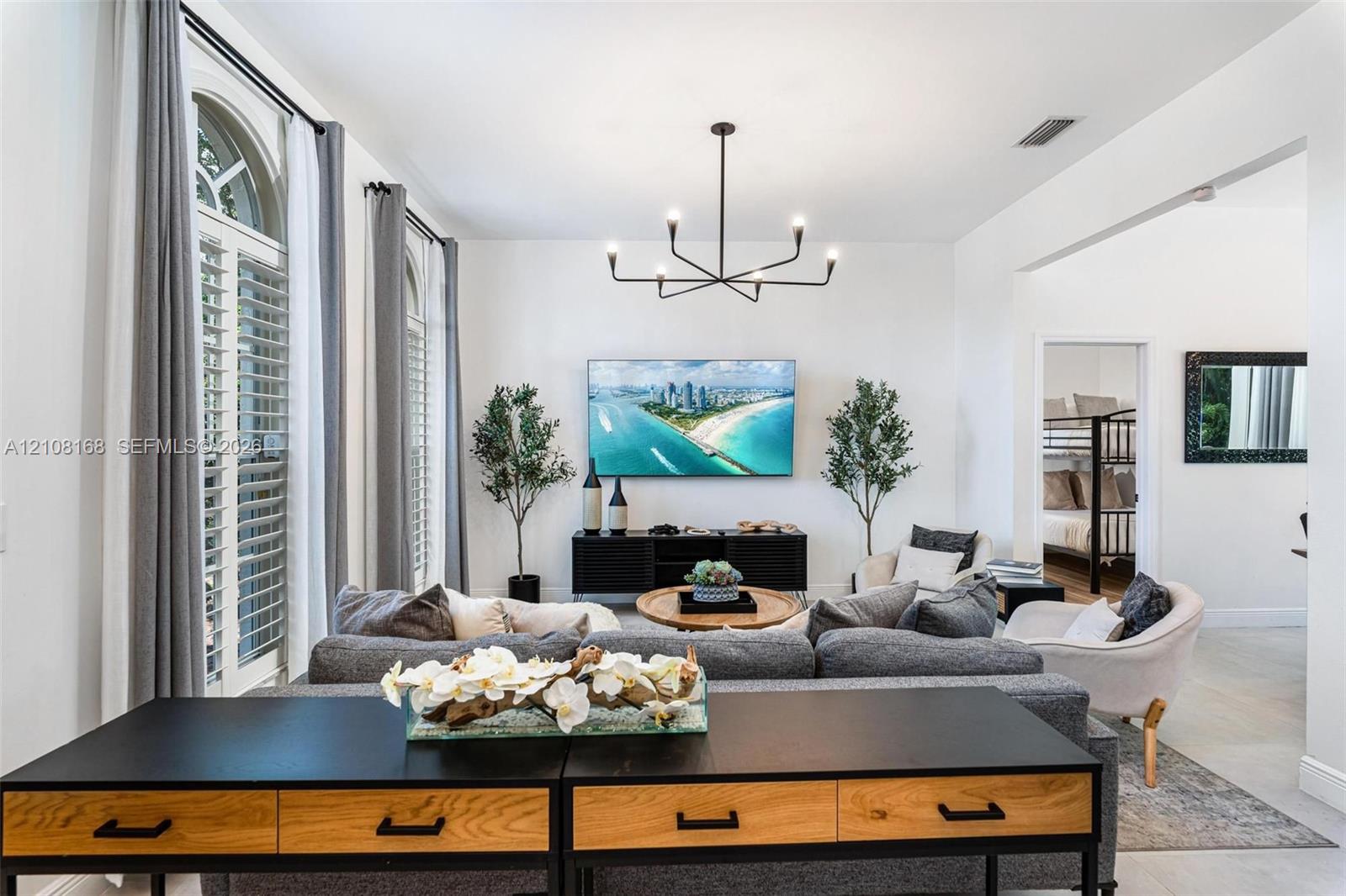 Living area featuring high ceilings, arched windows with plantation shutters, tile flooring, and a modern multi-arm chandelier