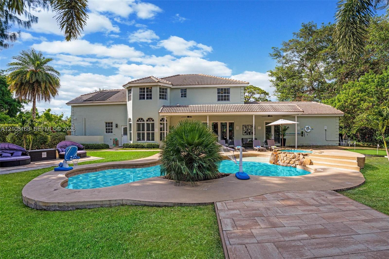 Backyard featuring a free-form swimming pool with a central island planter, raised stone-finished spa, expansive concrete pool decking, and a covered rear patio