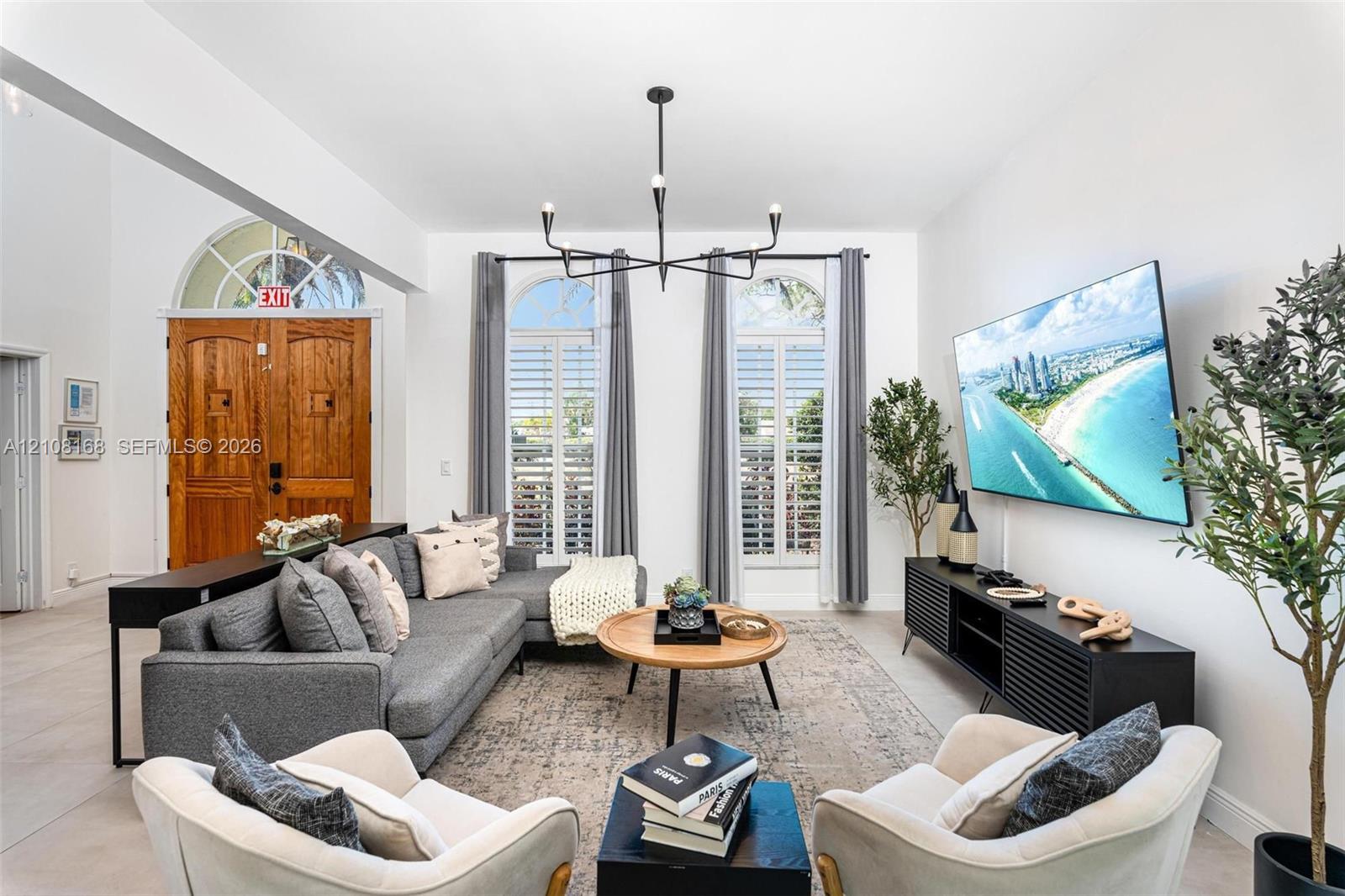 Living area featuring high ceilings, arched windows with plantation shutters, a multi-arm chandelier, and double wood entry doors with an arched transom window
