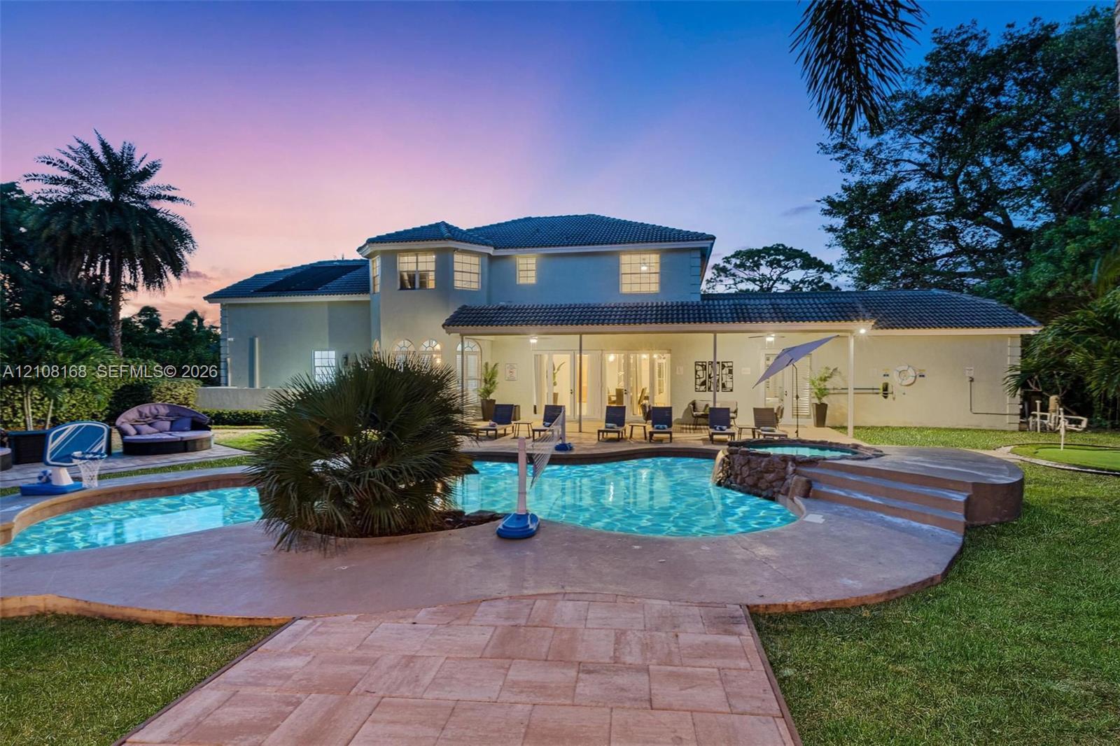 Two-story exterior featuring a hip roof, covered rear patio, freeform swimming pool, integrated spa, and stone-paver hardscaping