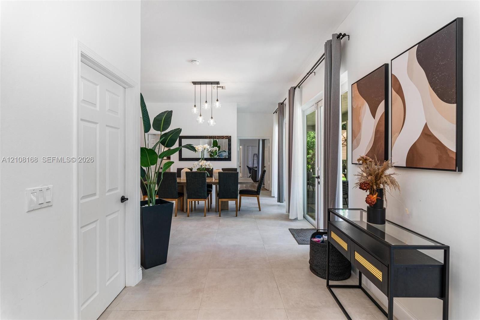 Large-format neutral floor tile, multi-light pendant chandelier, and sliding glass door with ceiling-mounted drapery hardware