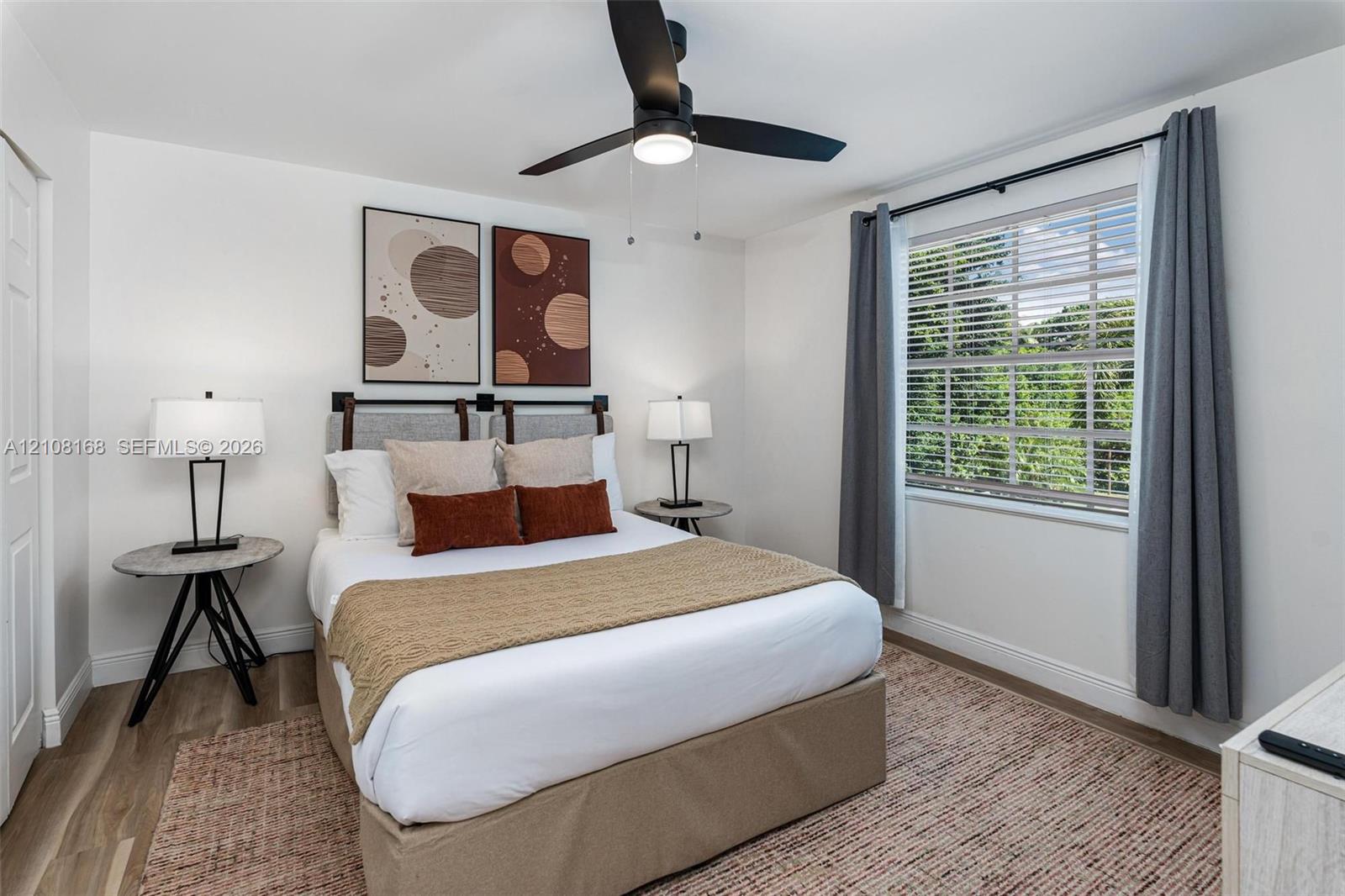 Bedroom featuring wood-finish flooring, a multi-pane window, and a matte black ceiling fan with an integrated light fixture