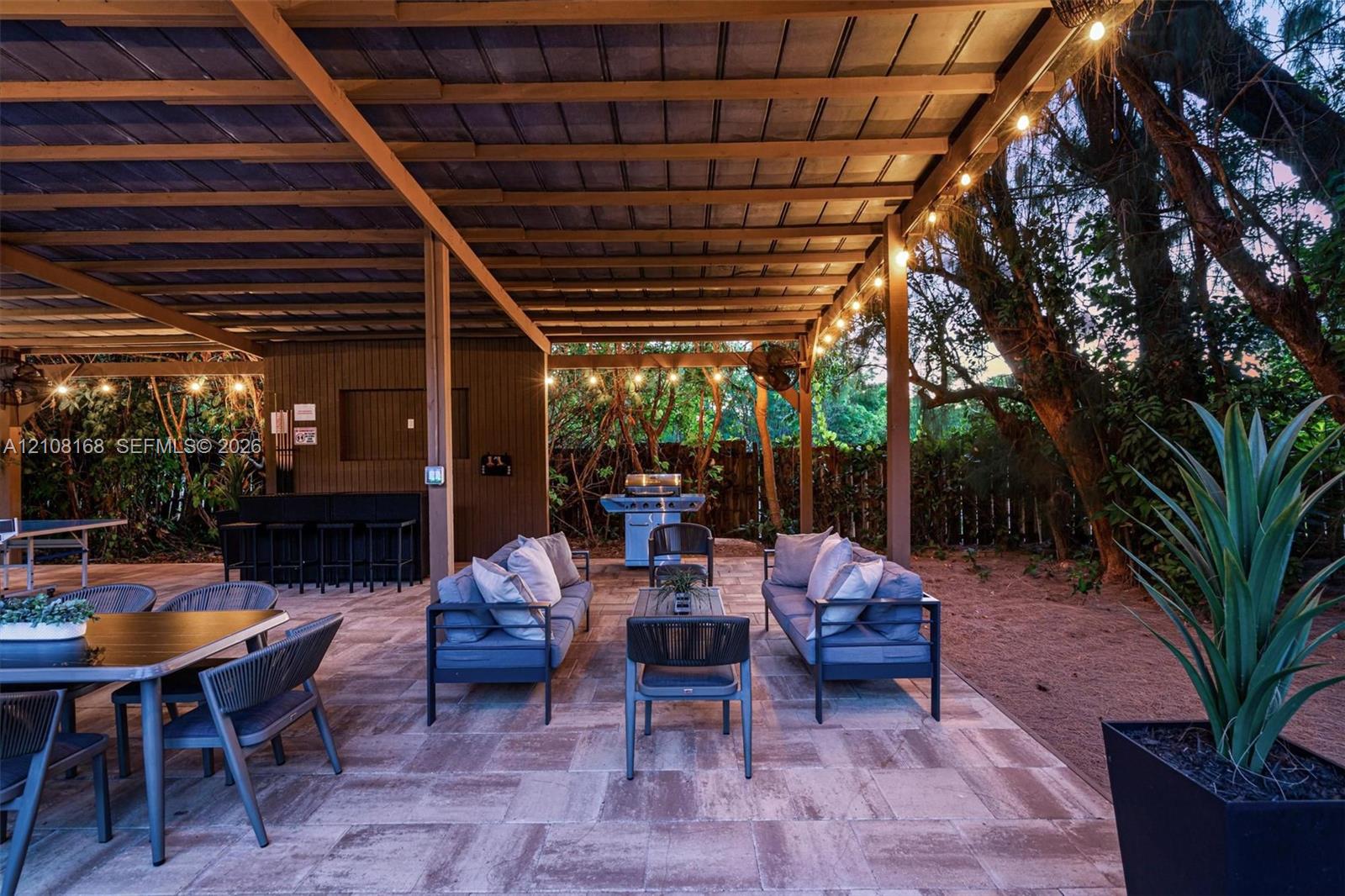 Covered outdoor patio featuring a wood-beam ceiling, stone-paver flooring, built-in bar, and mounted ceiling fans