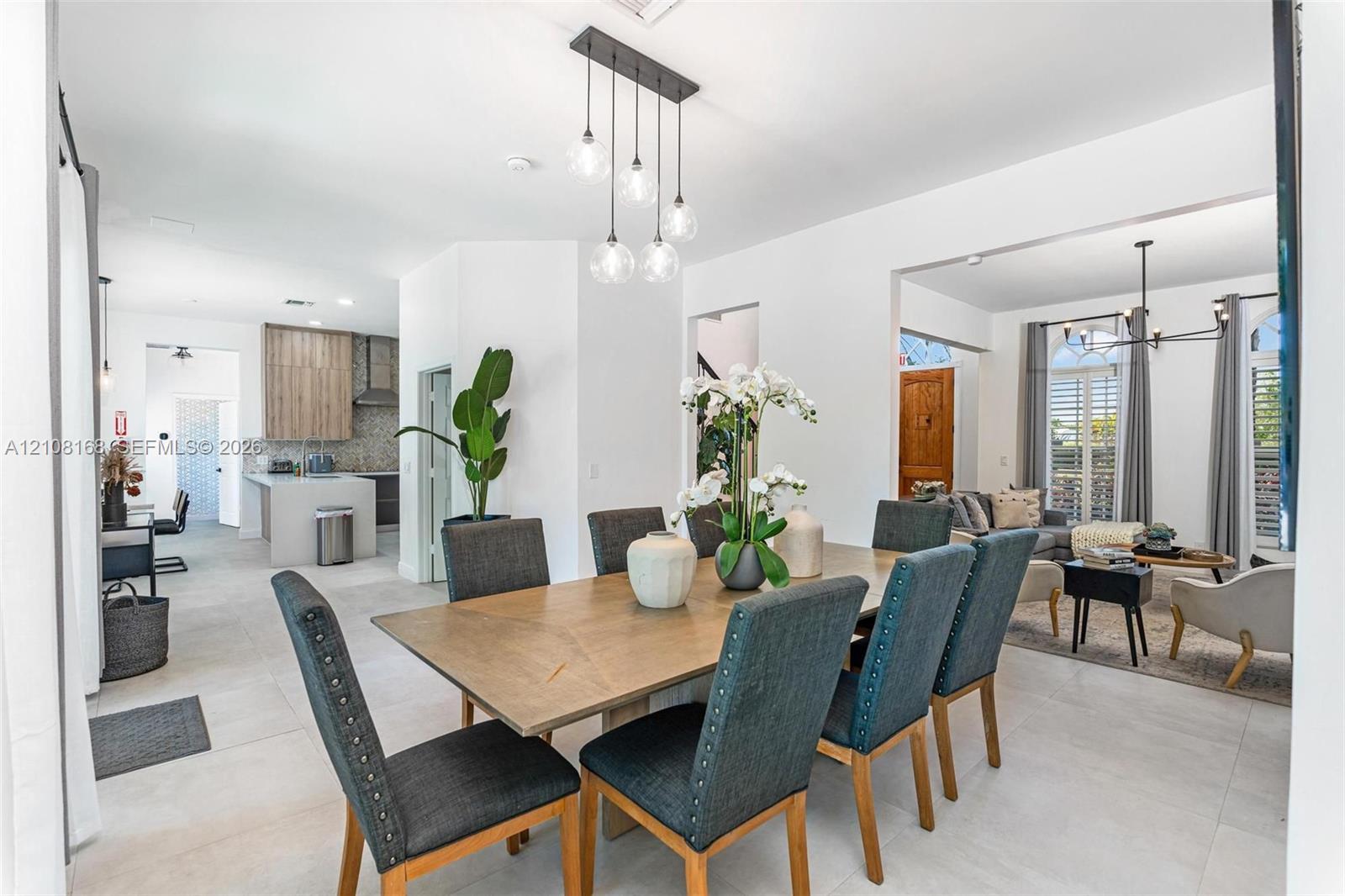 Open-concept interior featuring oversized light-toned floor tiling, a multi-light contemporary pendant fixture, and a minimalist kitchen island with clean-lined cabinetry