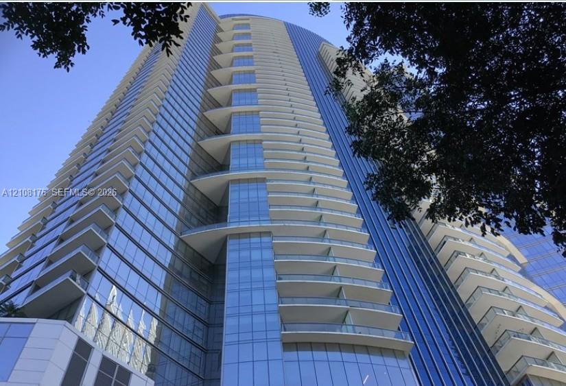 High-rise exterior featuring a blue glass curtain wall, curved architectural design, and private balconies with glass railings