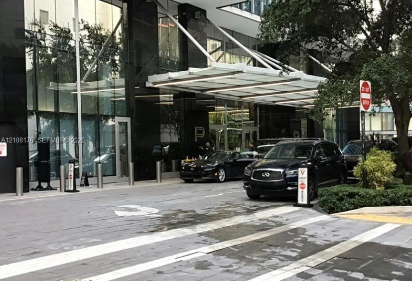 Contemporary building exterior featuring a polished black stone facade, expansive floor-to-ceiling glass paneling, and a cantilevered architectural canopy over a paved motor court