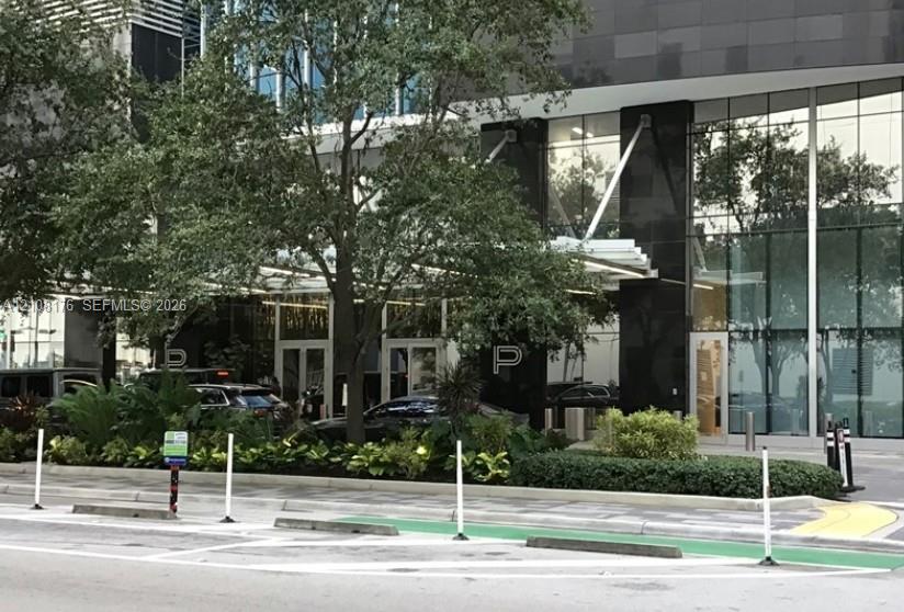 Modern glass-and-stone facade featuring a covered porte-cochre, floor-to-ceiling glass paneling, and polished dark stone accents