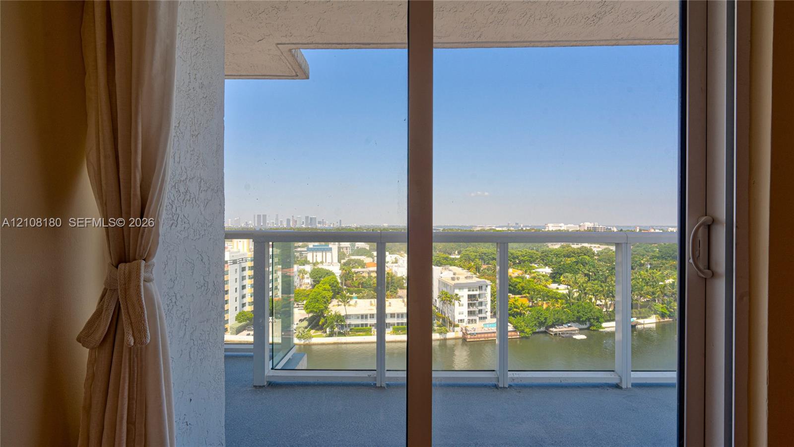 Private balcony featuring a glass-panel railing, sliding glass door entry, and water-front cityscape backdrop