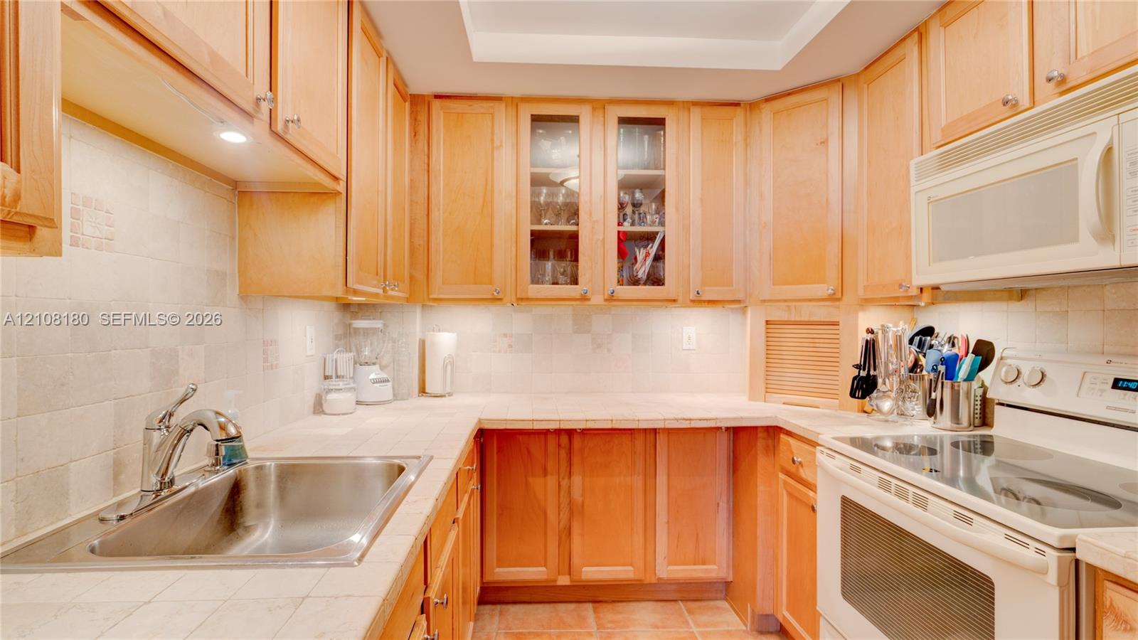 Kitchen featuring natural wood cabinetry, light-toned tile countertops, tiled backsplash, recessed ceiling lighting, and integrated over-the-range microwave