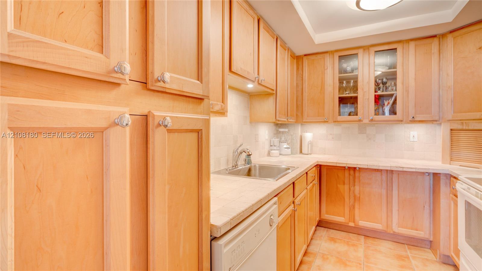 Kitchen featuring natural wood cabinetry, tile countertops, glass-front upper cabinet doors, under-cabinet lighting, and ceramic tile flooring