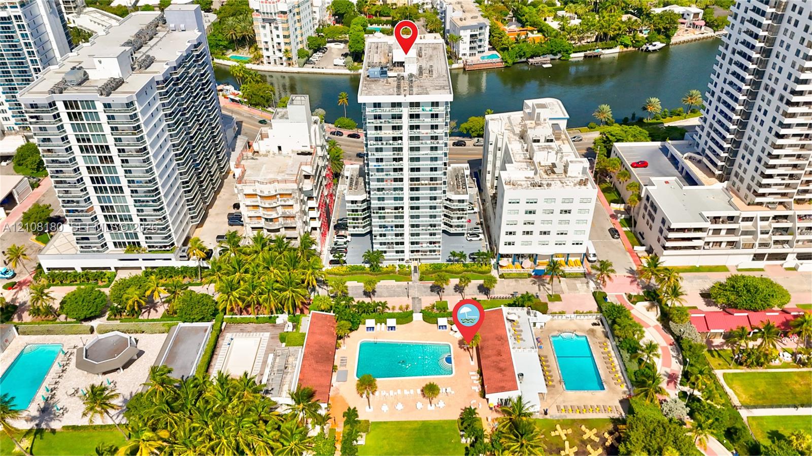 High-rise residential building featuring exterior balconies, a ground-level swimming pool, and tropical landscaping situated along a waterway High-rise residential building featuring exterior balconies, a ground-level swimming pool, and tropical landscaping situated along a waterway