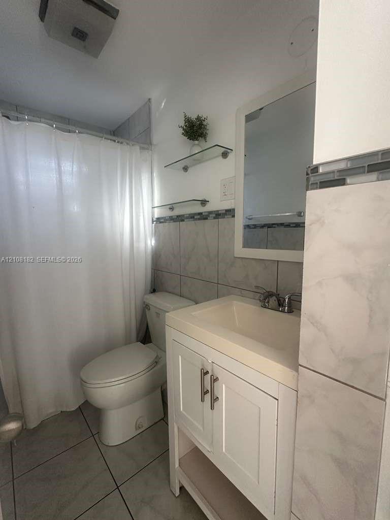 Bathroom featuring a white vanity cabinet with a stone-surface countertop, metal hardware, glass wall-mounted shelving, and tiled wall accents