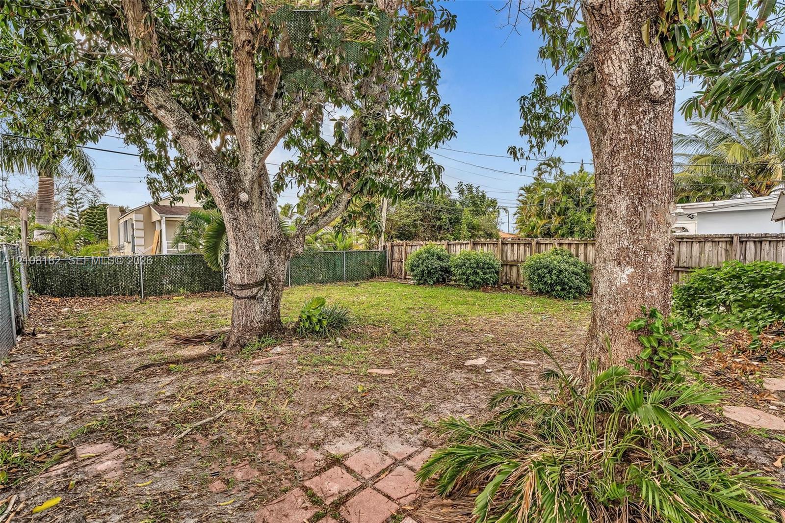 Backyard featuring mature trees, a wooden privacy fence, green lawn space, and a brick paver section