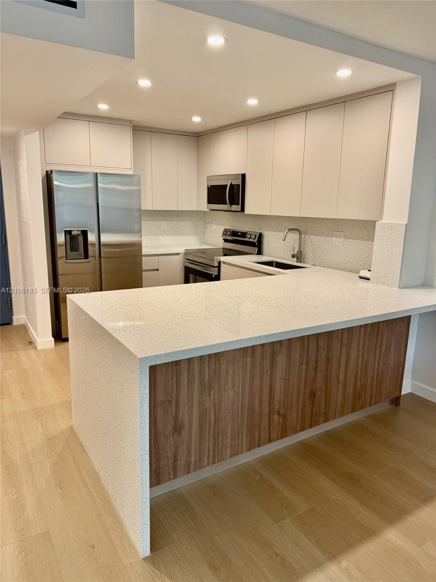 Kitchen featuring flat-panel cabinetry, light-toned stone-finish countertops, wood-finish island paneling, recessed lighting, and stainless steel appliances Kitchen featuring flat-panel cabinetry, light-toned stone-finish countertops, wood-finish island paneling, recessed lighting, and stainless steel appliances