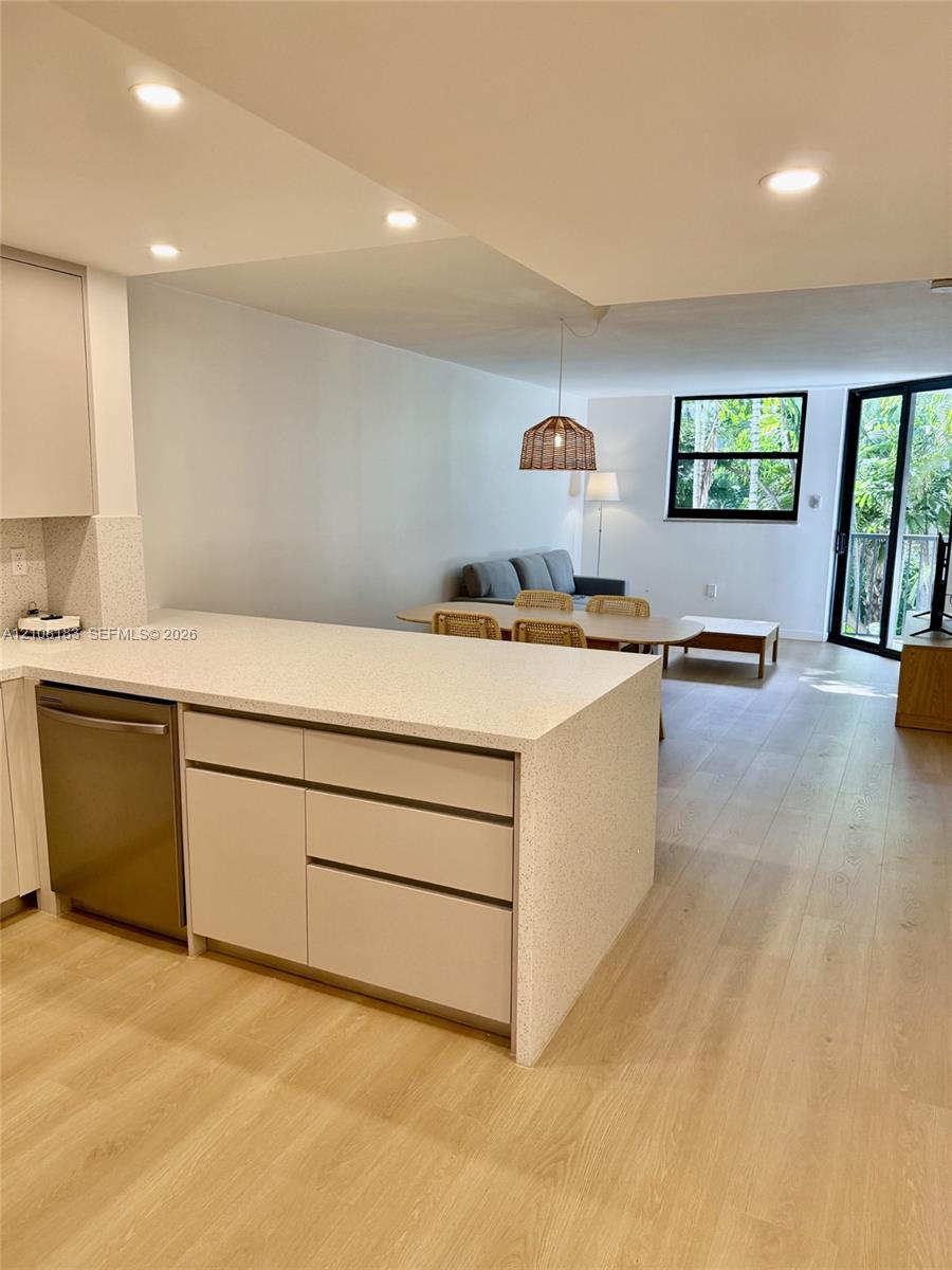 Kitchen featuring light-toned cabinetry, a stone-composite countertop island, stainless steel dishwasher, wood-finish flooring, and recessed ceiling lighting