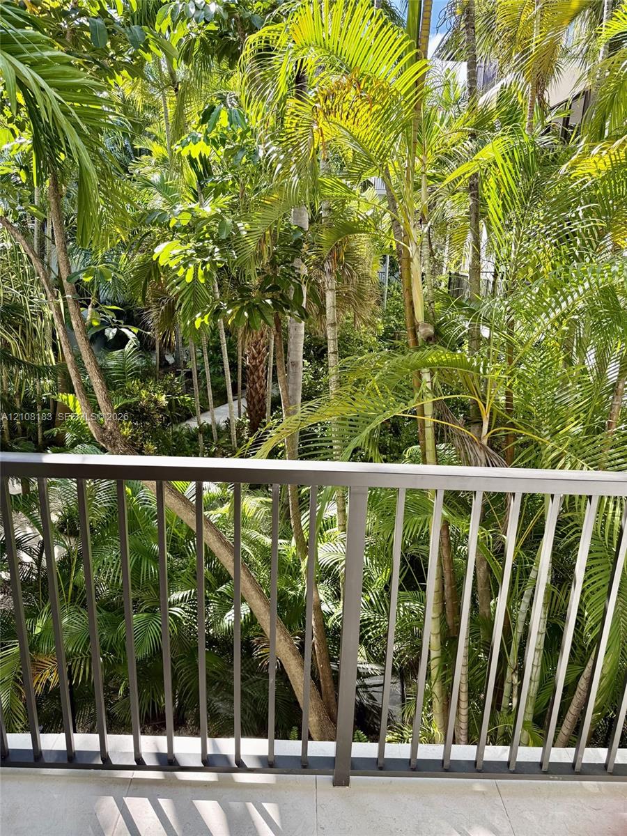 Balcony featuring a matte metal railing and stone-finish flooring overlooking dense, mature tropical landscaping