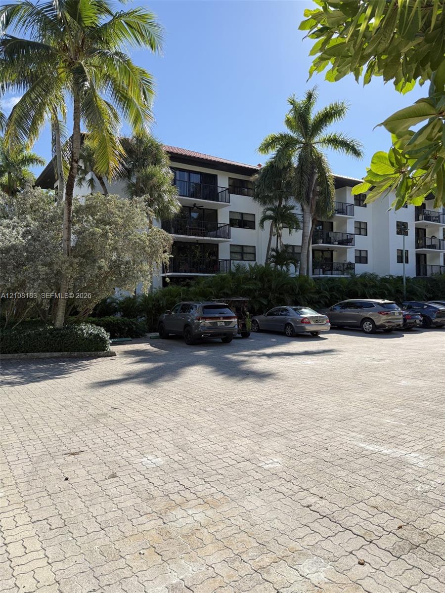 Multi-story residential building featuring private balconies, paver-stone parking area, and mature palm landscaping