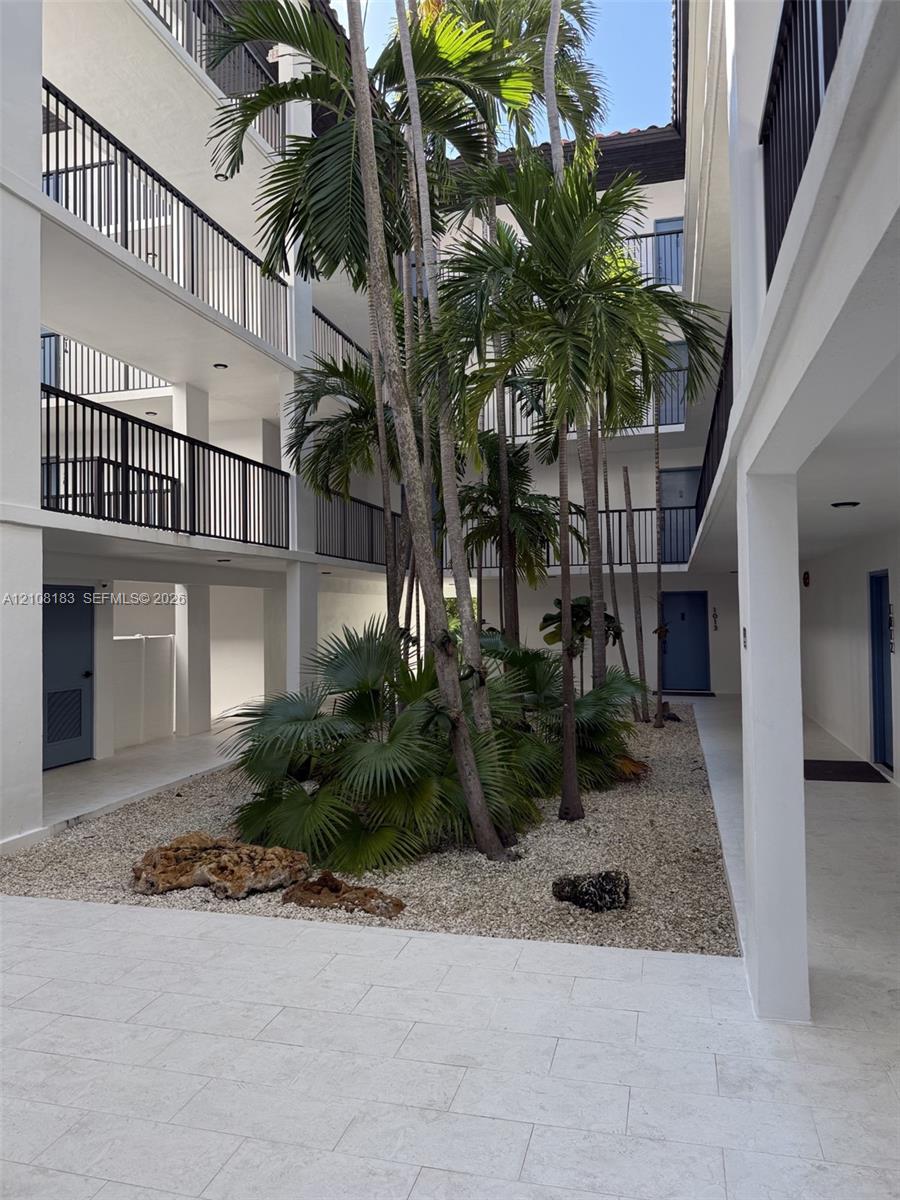 Central courtyard featuring stone-paved walkways, mature palm trees, decorative rock landscaping, and multi-level balconies with black metal railings
