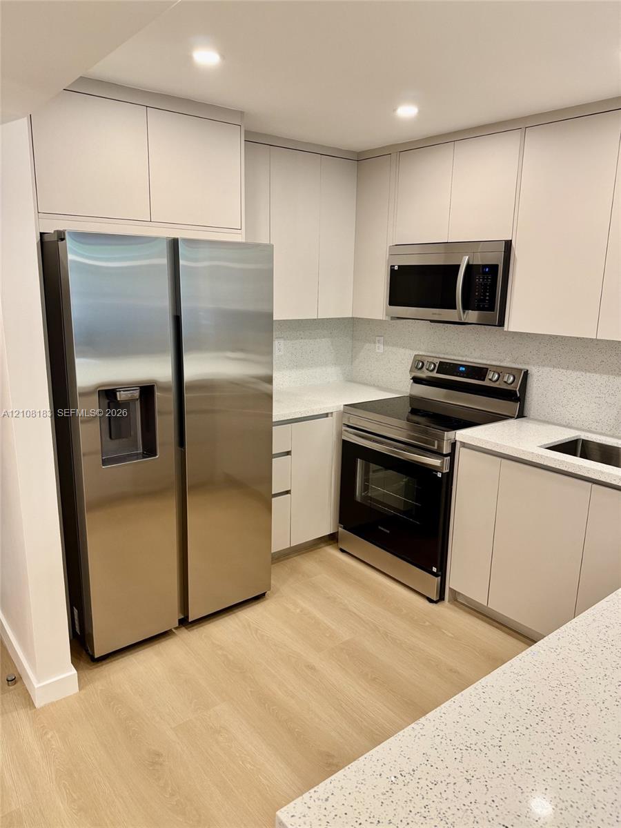 Kitchen featuring flat-panel cabinetry, light-toned countertops, wood-finish flooring, and stainless steel appliances including a side-by-side refrigerator, built-in microwave, and range