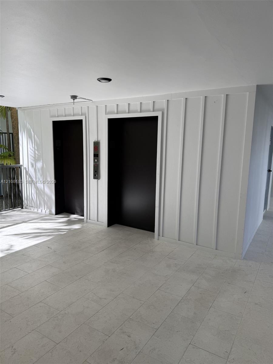 Dual elevator access featuring matte black entry portals, set against a board-and-batten accent wall with stone tile flooring and recessed ceiling lighting
